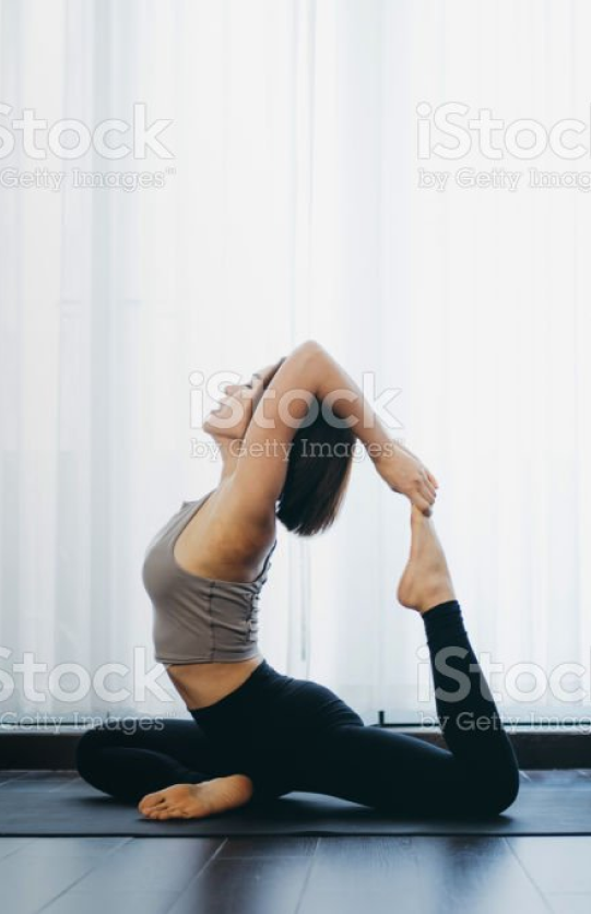 Woman on floor doing yoga pose infront of white curtains